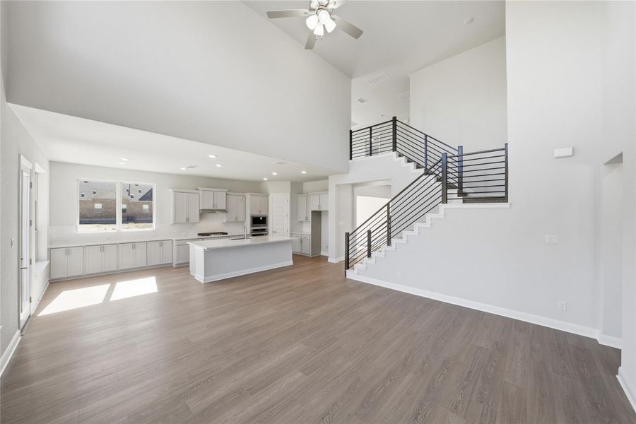 Unfurnished living room featuring a towering ceiling, stairway, dark wood-style floors, ceiling fan, and recessed lighting