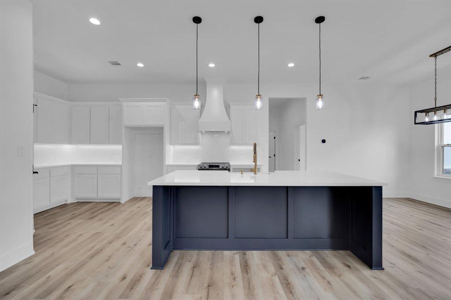 Kitchen featuring custom exhaust hood, white cabinetry, a large island with sink, and light hardwood / wood-style floors