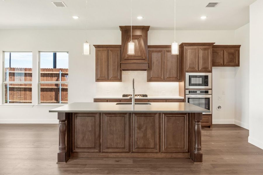 Kitchen with large dark wood island, matching cabinets, custom range hood, and stainless steel double ovens Kitchen with large dark wood island, matching cabinets, custom range hood, and stainless steel double ovens