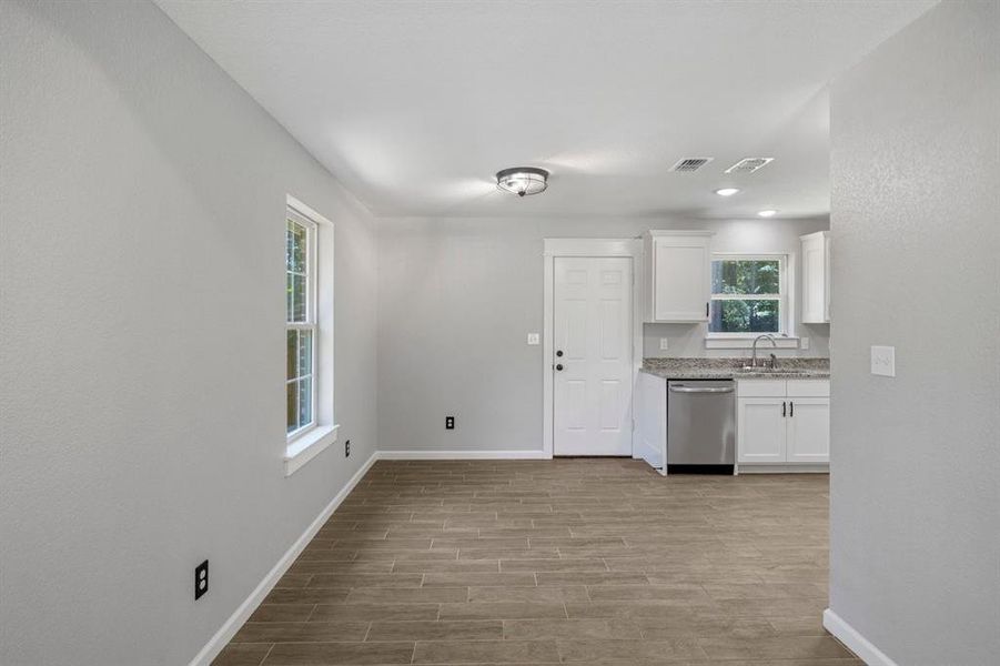 Kitchen with white cabinets, stainless steel dishwasher, light stone countertops, and wood tiled floors Kitchen with white cabinets, stainless steel dishwasher, light stone countertops, and wood tiled floors