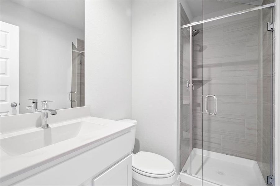 This private bath features tile flooring, shower with tile surround, light stained wood cabinets, beautiful light countertops, mirror, dark, sleek fixtures and modern finishes.