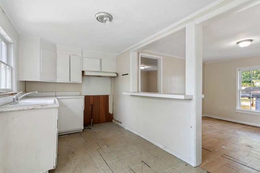 Kitchen with white cabinetry, a sink, crown molding, light flooring, and light countertops