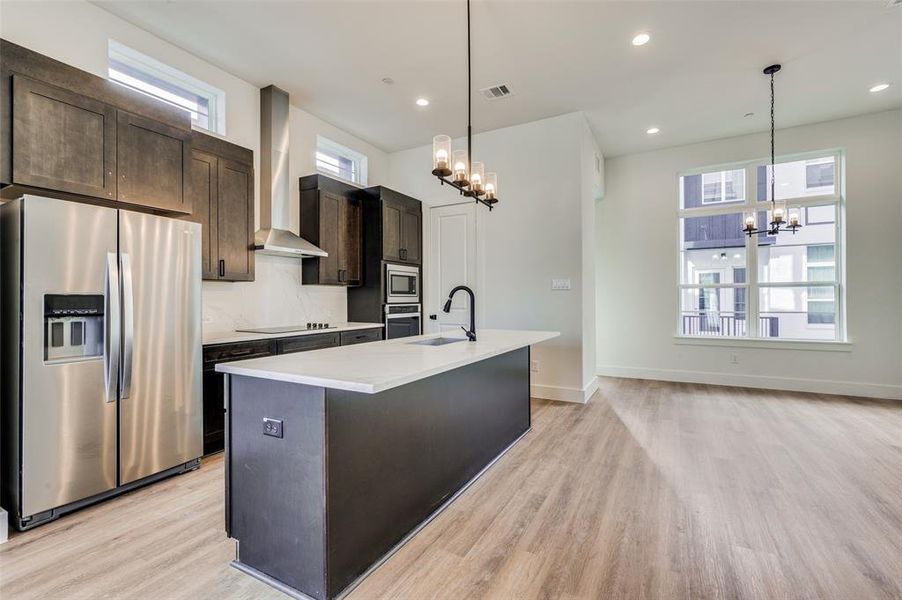 Kitchen featuring stainless steel appliances, a healthy amount of sunlight, light hardwood / wood-style flooring, and a kitchen island with sink