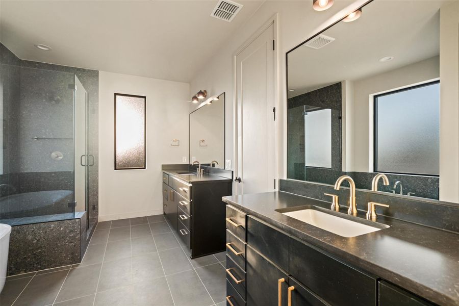 Dual vanities with sophisticated hardware and a frameless glass shower define this contemporary primary bathroom.