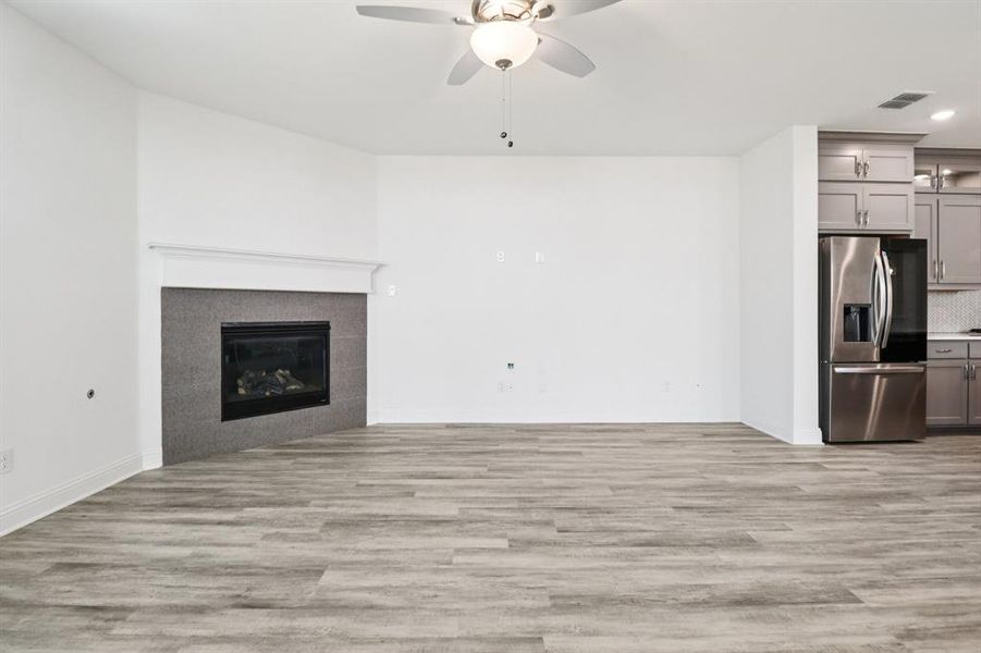Unfurnished living room featuring light wood finished floors, a ceiling fan, a tiled fireplace, and recessed lighting Unfurnished living room featuring light wood finished floors, a ceiling fan, a tiled fireplace, and recessed lighting
