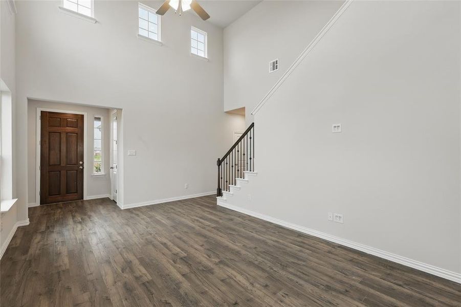 Entryway with ceiling fan, plenty of natural light, dark wood-style flooring, stairway, and a towering ceiling