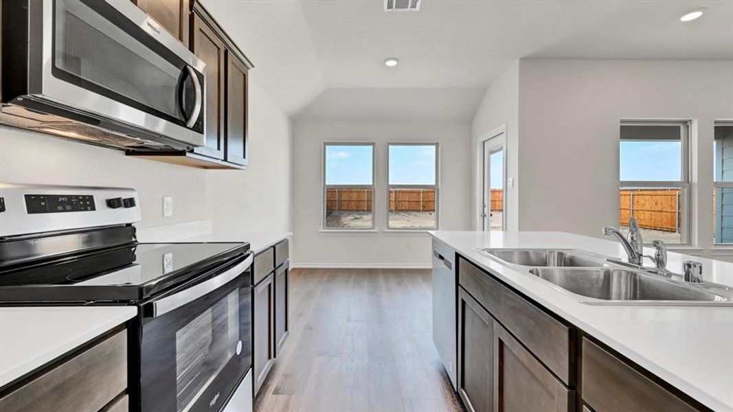 Contemporary kitchen featuring stainless steel appliances, white countertops, wood-finish flooring, dark wood cabinetry, and recessed lighting