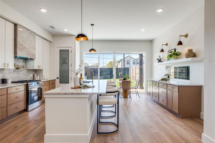 Kitchen with light stone countertops, decorative light fixtures, stainless steel gas range oven, a kitchen bar, and tasteful backsplash