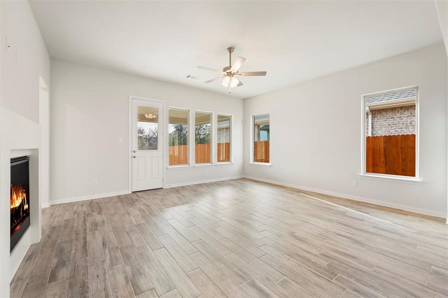 Unfurnished living room featuring a lit fireplace, light wood-type flooring, and a ceiling fan