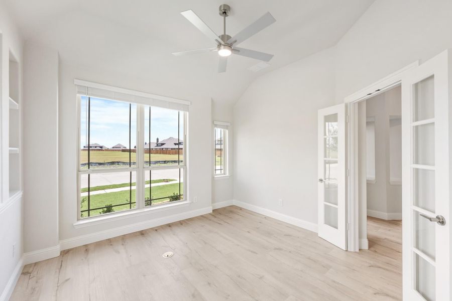 Empty room with vaulted ceiling, ceiling fan, light wood floors, and French doors leading to a closet
