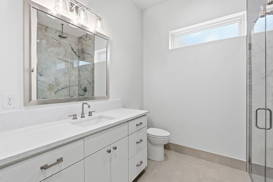 A glass-enclosed shower alongside a modern stone-topped vanity anchors this bath.