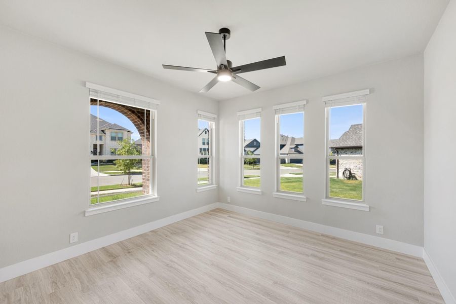 Empty room with light wood floors, ceiling fan, and four windows overlooking a neighborhood