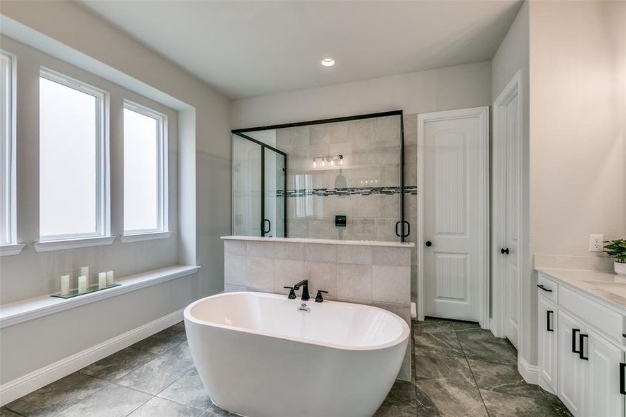 Bathroom with tile flooring, vanity, and independent shower and free standing bathtub.