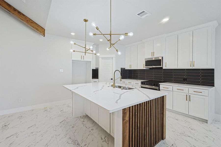 Kitchen featuring pendant lighting, sink, stainless steel appliances, light stone countertops, and an island with sink