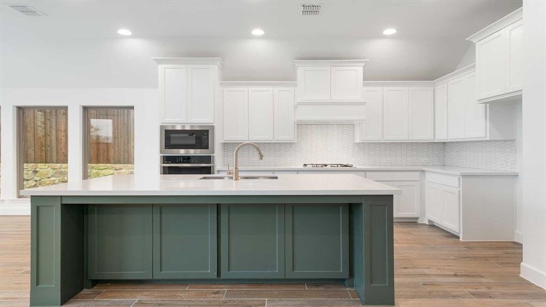 Kitchen with light hardwood / wood-style flooring, white cabinets, a center island with sink, and appliances with stainless steel finishes