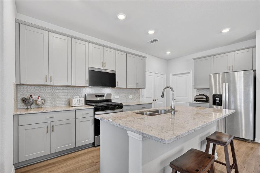 Kitchen featuring stainless steel appliances, light stone counters, light wood-style floors, backsplash, and a breakfast bar