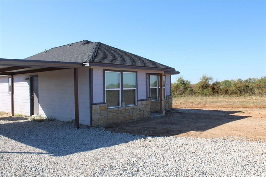 View of home's exterior with a shingled roof and stone siding