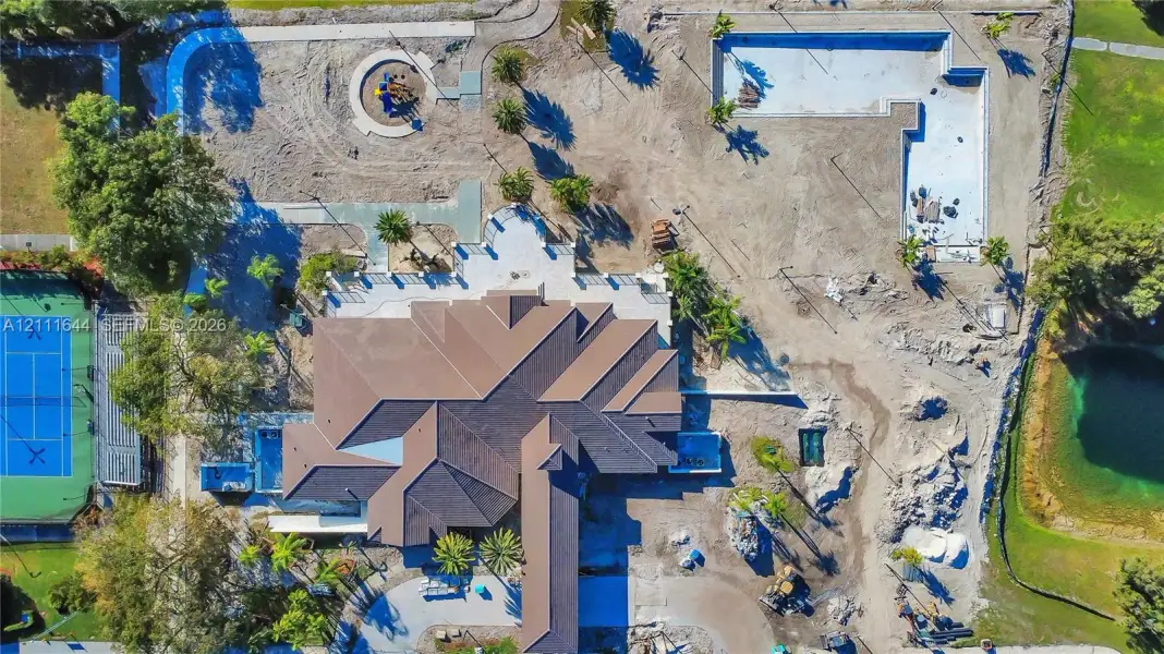 Aerial view of a sprawling property featuring a multi-gabled roofline, a dedicated tennis court, a large pool structure, and surrounding grounds Aerial view of a sprawling property featuring a multi-gabled roofline, a dedicated tennis court, a large pool structure, and surrounding grounds