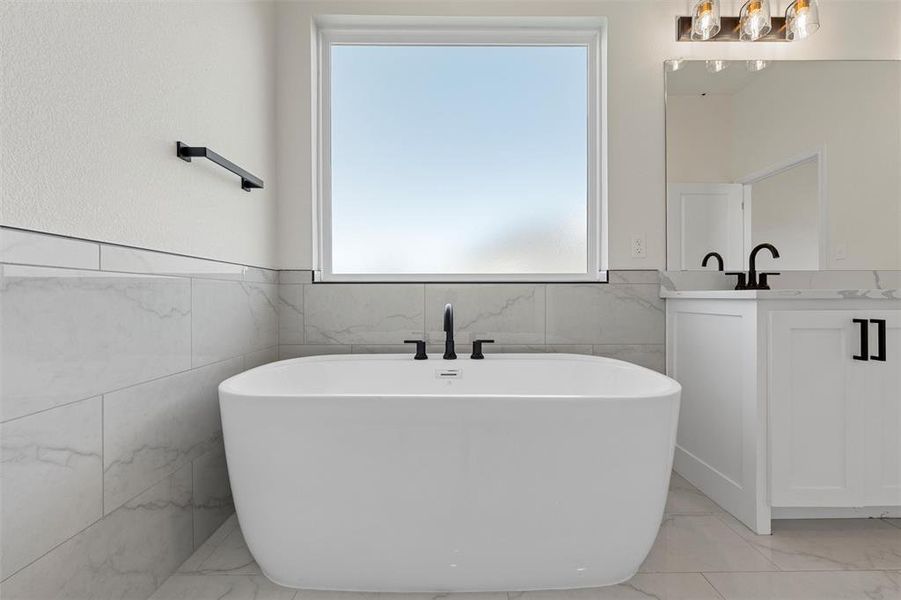 Full bathroom featuring vanity, tile walls, a freestanding tub, light marble finish flooring, and a wainscoted wall