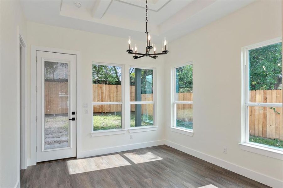 Unfurnished dining area featuring dark wood-style flooring, a chandelier, and a tray ceiling