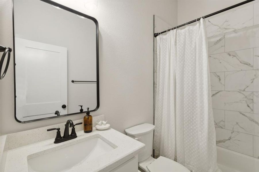 Bathroom featuring an undermount sink, a light-toned countertop, a black-framed mirror, a black faucet, and white subway tile in the shower