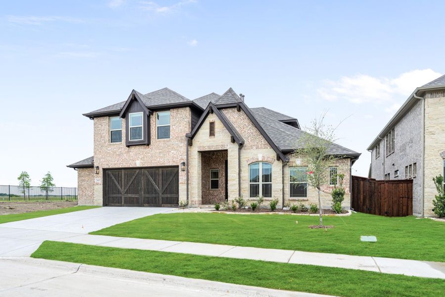 Two-story brick home with two-car garage, arched entry, and green front lawn