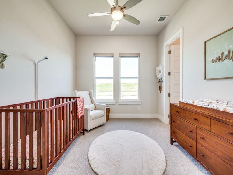 Bedroom featuring light carpet, a crib, baseboards, and a ceiling fan