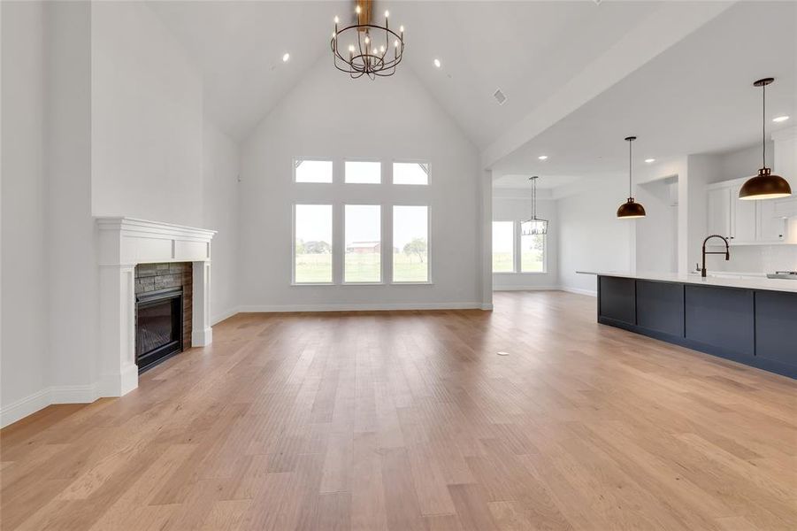 Unfurnished living room with high vaulted ceiling, sink, light hardwood / wood-style flooring, and a notable chandelier