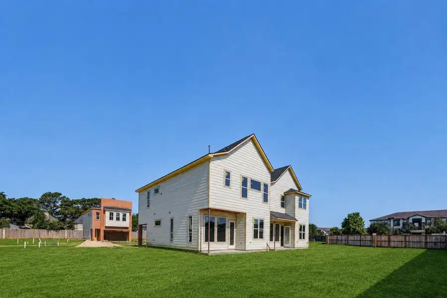 Wide rear-side exterior view capturing the two-story profile, light siding, rear doors, window placement, and expansive lawn area. This perspective emphasizes the home’s modern new-construction design, outdoor space, and neighborhood layout, while showing how the homes are positioned within the developing boutique community. Wide rear-side exterior view capturing the two-story profile, light siding, rear doors, window placement, and expansive lawn area. This perspective emphasizes the home’s modern new-construction design, outdoor space, and neighborhood layout, while showing how the homes are positioned within the developing boutique community.