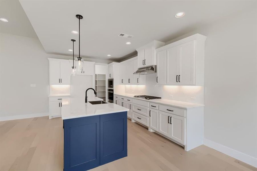 Kitchen featuring a blue island with an integrated sink, white shaker cabinetry, stainless steel appliances, and light wood-finish flooring
