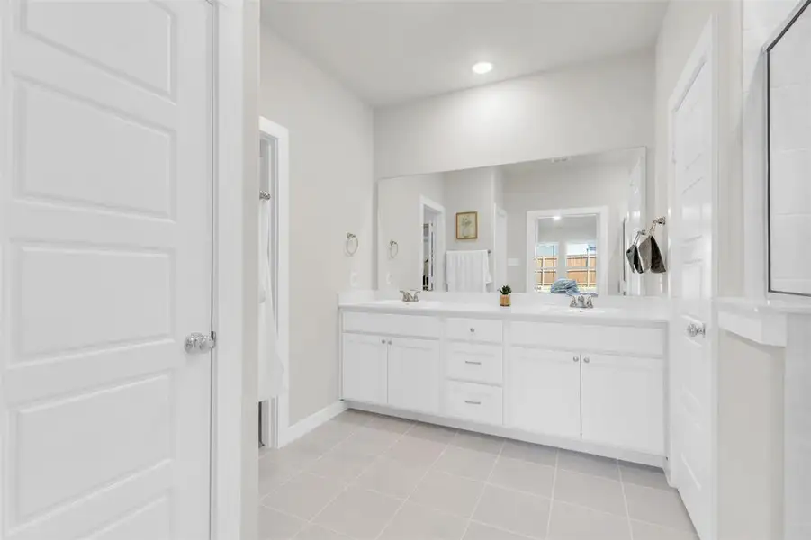 Ensuite bathroom with ensuite bathroom, baseboards, a sink, double vanity, and tile patterned flooring