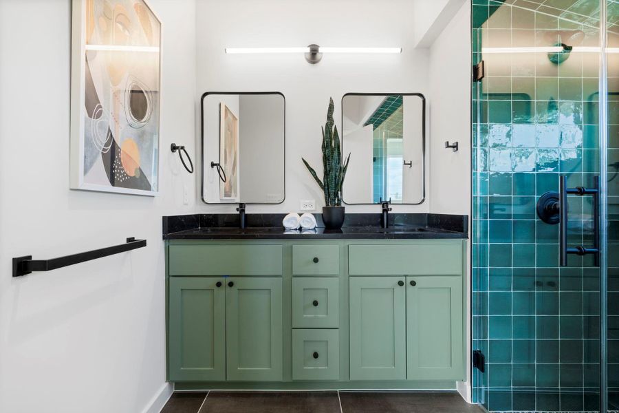 Bathroom with double vanity, a shower stall, and dark tile patterned floors
