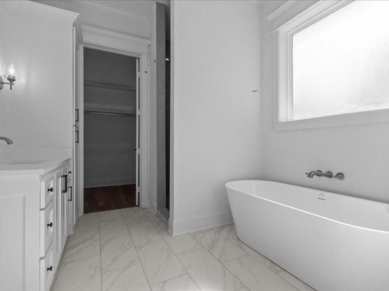 Full bath featuring vanity, a freestanding bath, light marble finish floors, and a closet