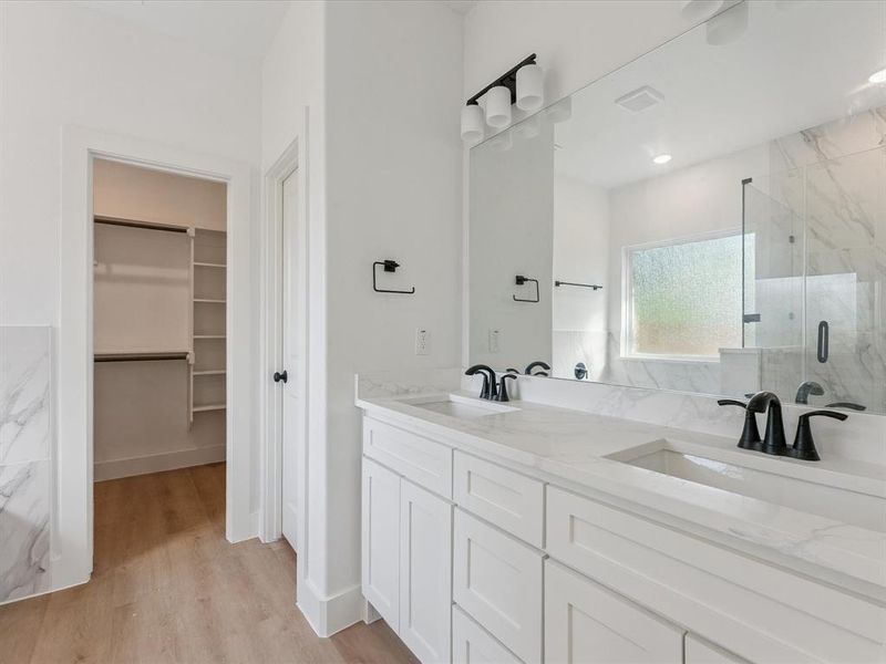 Full bathroom featuring a spacious closet, a marble finish shower, double vanity, and light wood-style floors