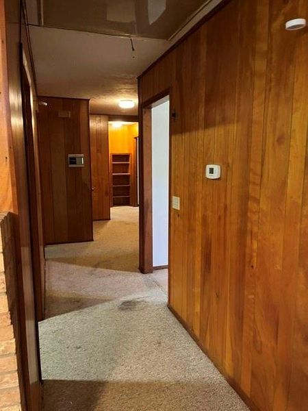 Hallway featuring wood paneling, carpeted flooring, and flush-mounted ceiling lighting Hallway featuring wood paneling, carpeted flooring, and flush-mounted ceiling lighting