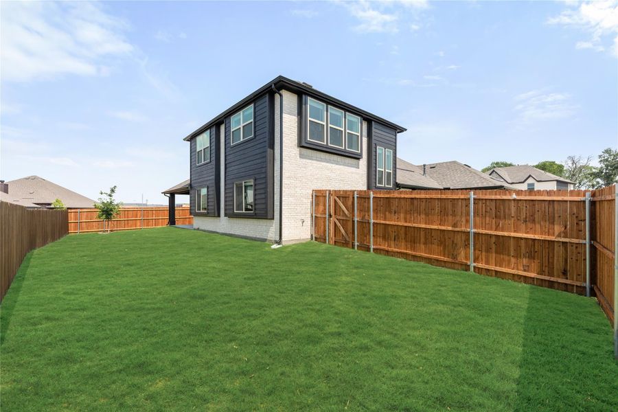 Two-story home with dark siding and brick exterior, large grassy backyard with wood privacy fence