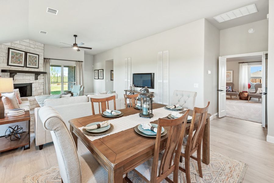 Open-concept dining area with wood table and chairs flowing into living room with stone fireplace and ceiling fan Open-concept dining area with wood table and chairs flowing into living room with stone fireplace and ceiling fan