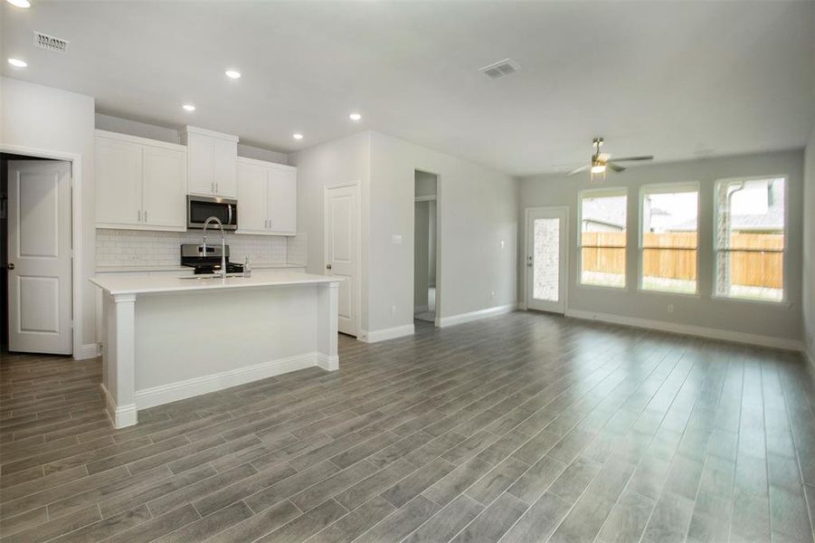 Kitchen with stainless steel microwave, ceiling fan, light countertops, backsplash, and a center island with sink Kitchen with stainless steel microwave, ceiling fan, light countertops, backsplash, and a center island with sink