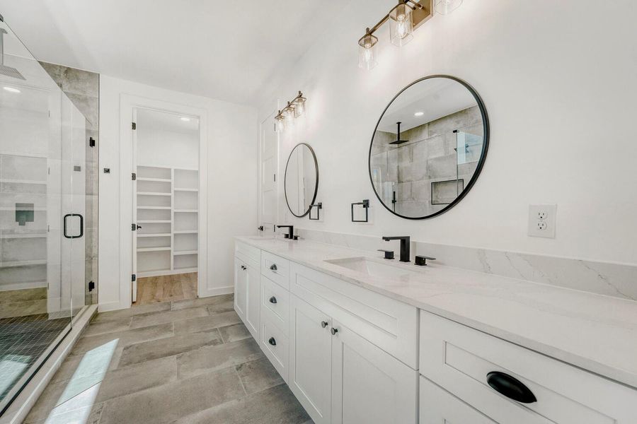 Full bath featuring a shower stall, double vanity, and a spacious closet