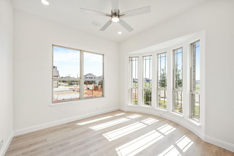 Bright empty room with large bay windows, ceiling fan, and light hardwood floors