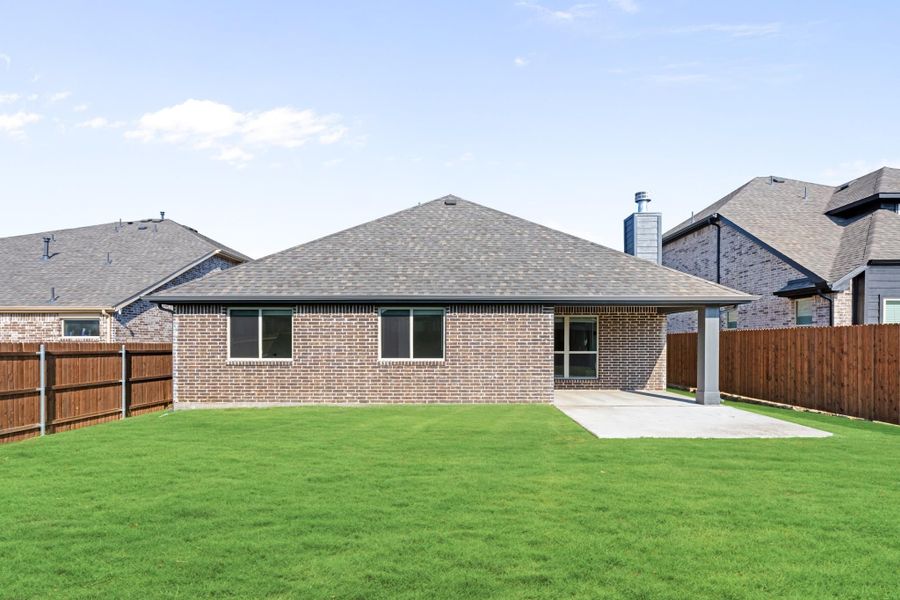 Brick home rear exterior with covered patio, concrete pad, green lawn, and wood privacy fence. Brick home rear exterior with covered patio, concrete pad, green lawn, and wood privacy fence.
