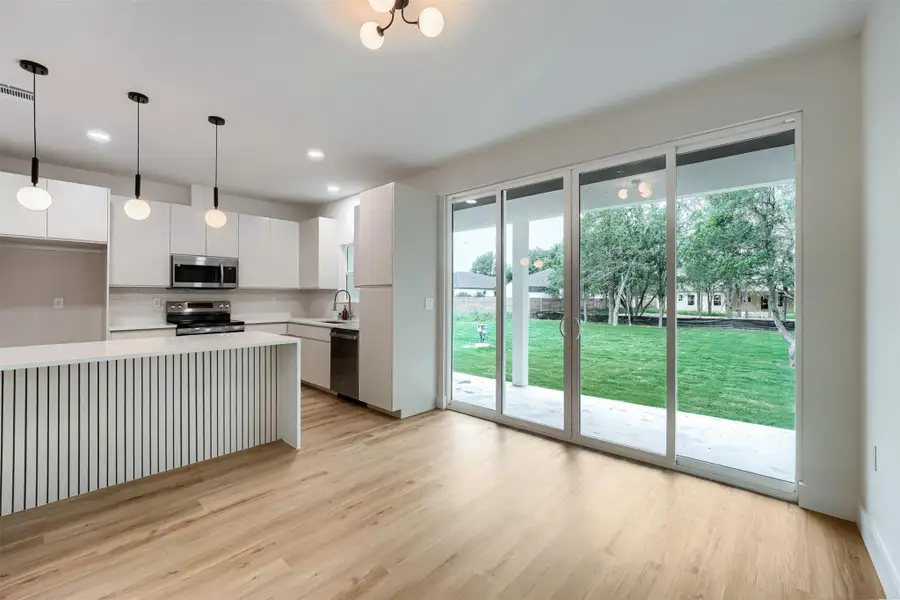 Kitchen and living area featuring wood-finish flooring, white cabinetry, stainless steel appliances, and a central island with decorative paneling