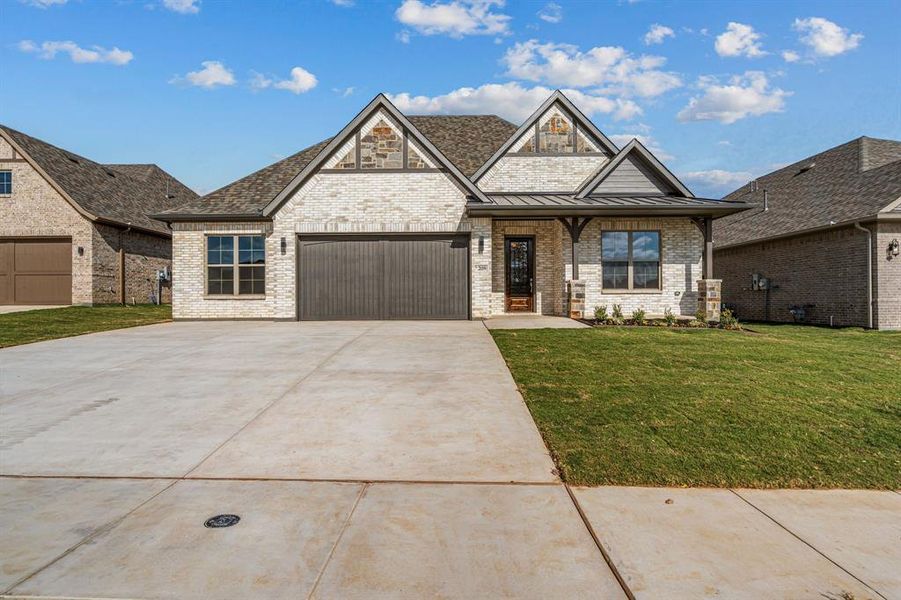 View of front of home featuring brick siding, a front yard, driveway, a standing seam roof, and covered porch
