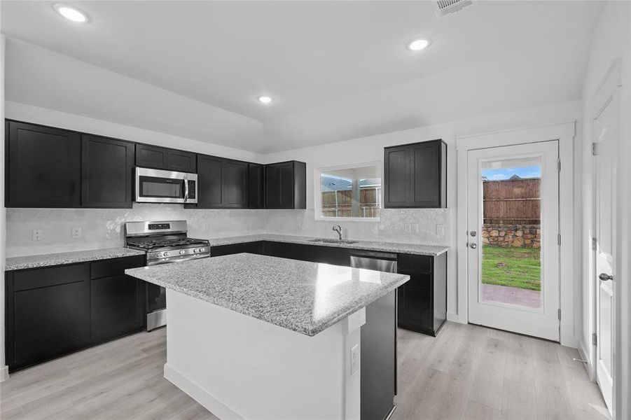 Kitchen with stainless steel appliances, light wood-style floors, light stone counters, and a kitchen island