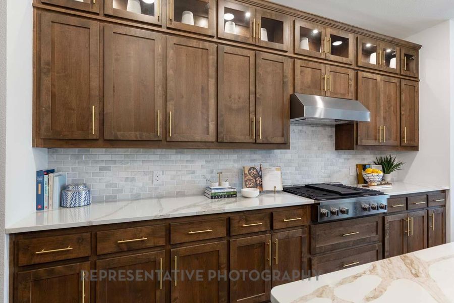 Kitchen with ventilation hood, stainless steel gas cooktop, tasteful backsplash, and light stone counters Kitchen with ventilation hood, stainless steel gas cooktop, tasteful backsplash, and light stone counters