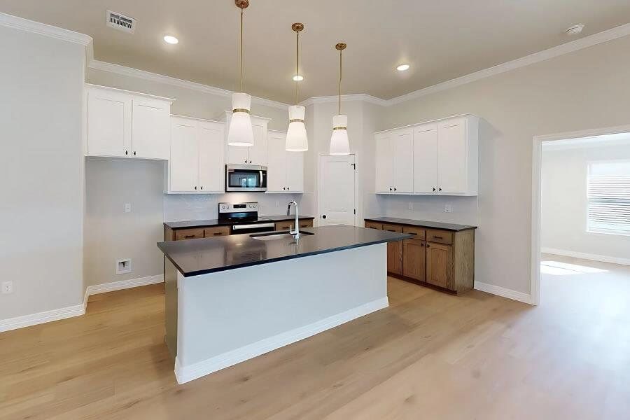 Kitchen featuring a kitchen island with sink, white cabinets, appliances with stainless steel finishes, light wood finished floors, and ornamental molding