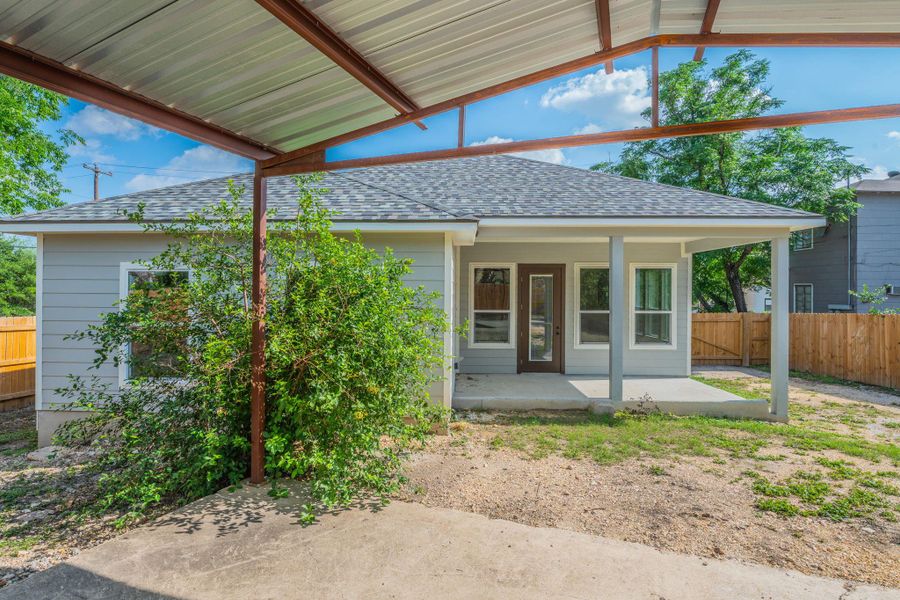 Rear exterior featuring a covered patio, light gray siding, dark shingle roofing, and a wooden fence
