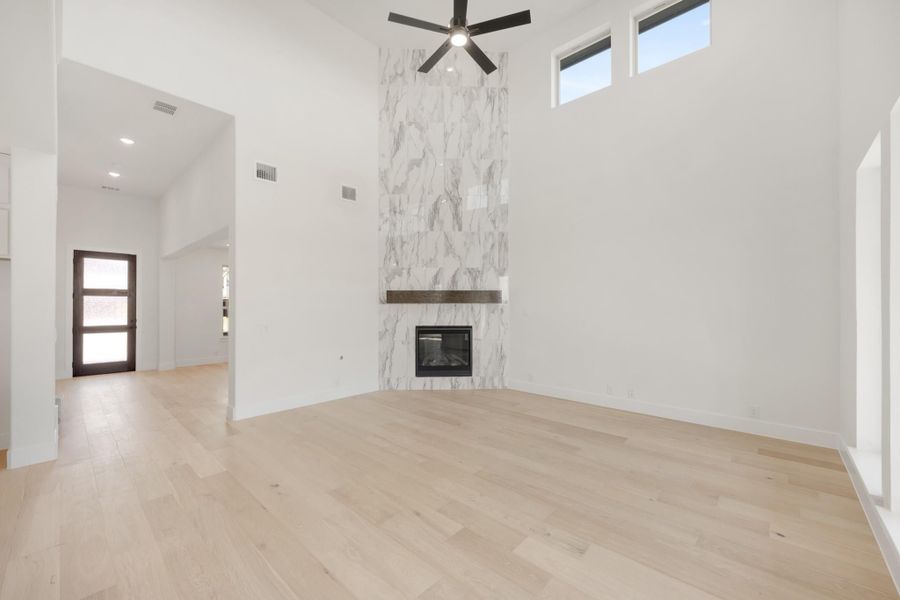 Open living room with tall marble fireplace surround, ceiling fan, and light hardwood floors