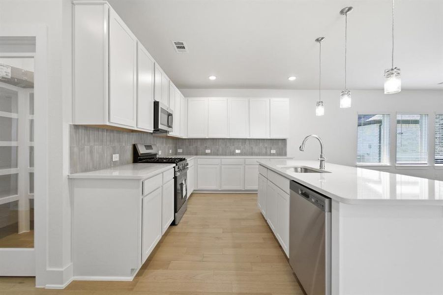 Modern kitchen featuring abundant white cabinetry, stainless steel appliances, light wood-finish flooring, a substantial center island with integrated sink, and an elegant tile backsplash