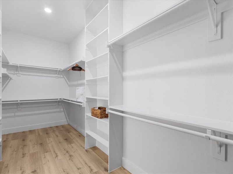 Spacious walk-in closet featuring extensive built-in shelving, multiple hanging rods, recessed ceiling lighting, and wood-finish flooring